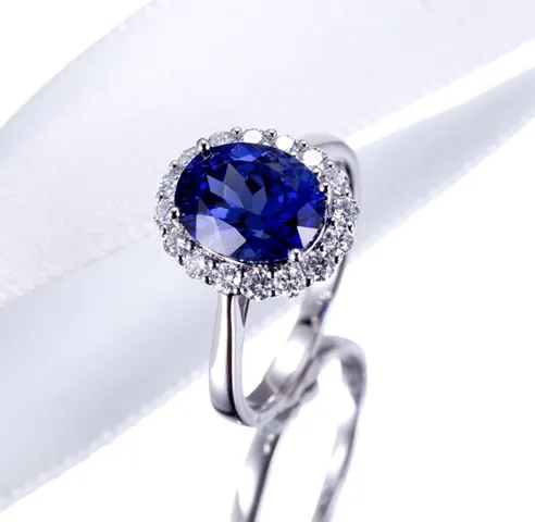 A sapphire ring with a diamond halo, photographed on white satin