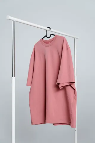 A dusty pink oversized T-shirt on a hanger, on a clothes rail